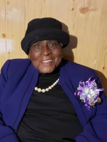 Elderly woman smiling in purple attire.