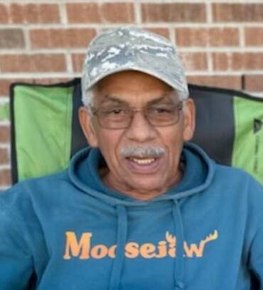 Man in hoodie and cap sitting outside.
